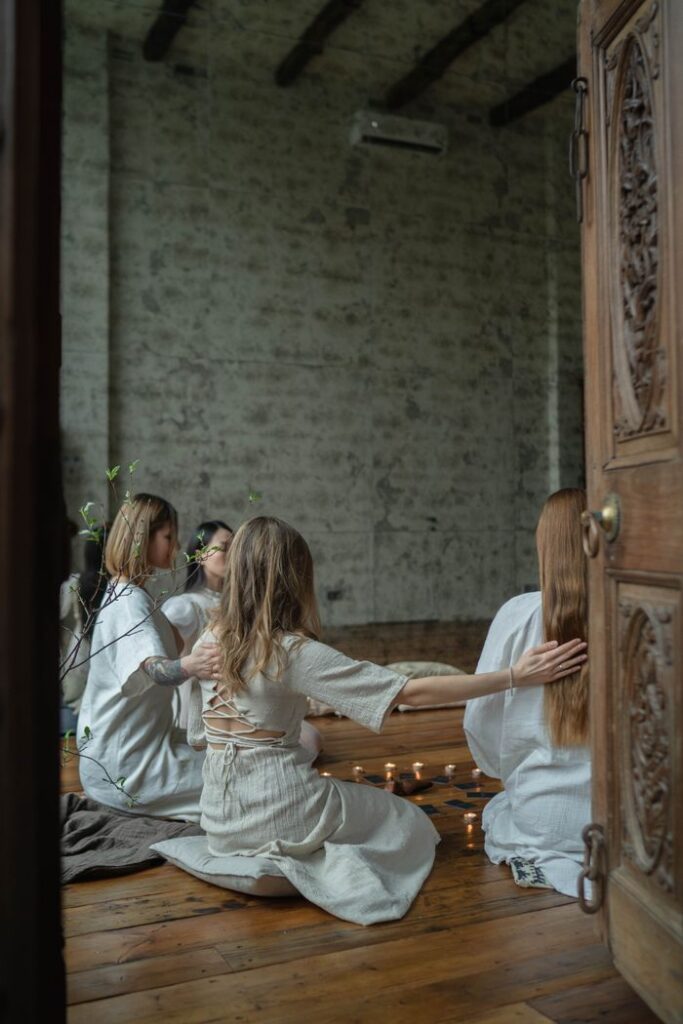 Women in peaceful meditation circle with candles inside a rustic room.