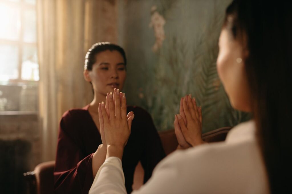 Two women practicing a calming hand exercise in a softly lit room, focusing on mindfulness and relaxation.