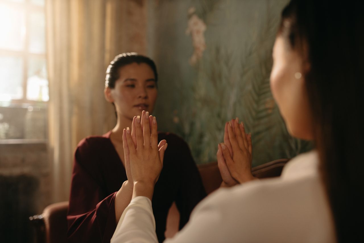 Two women practicing a calming hand exercise in a softly lit room, focusing on mindfulness and relaxation.